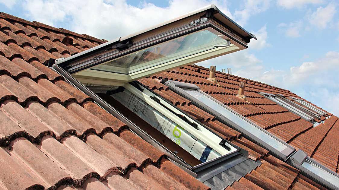 Ein geöffnetes Designo R8 Klapp-Schwingfenster auf einem Dach mit weiteren geschlossenen Dachfenstern